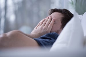 Mann mit Schlafstörung, hält sich die Hände vor das Gesicht.
