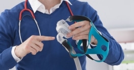 Ein Arzt zeigt die Schlafmaske eines CPAP-Beatmungsgeräts